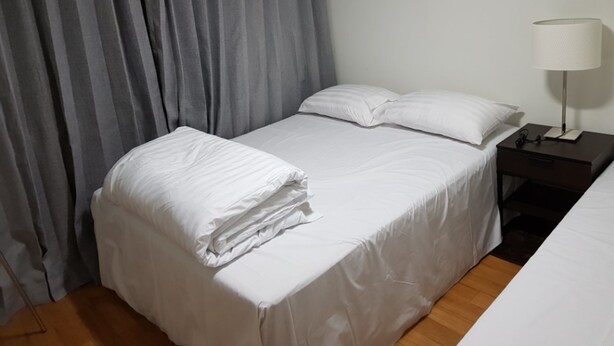 A neatly made bed with white linens, a bedside table with a lamp, and grey curtains. - Galaxy Gangnam 2 (Seoul)