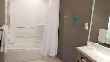Casa de banho moderna com banheira, cortina de chuveiro, barra de apoio, porta-toalhas, lavatório com artigos de higiene pessoal e espelho.
