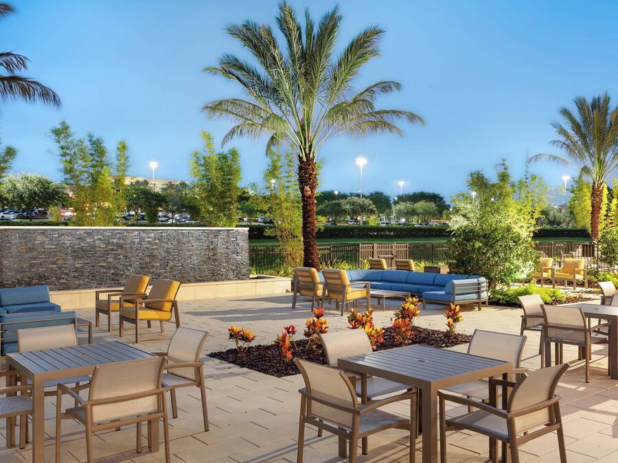 An outdoor patio with seating and tables, palm trees, and a stone wall.
