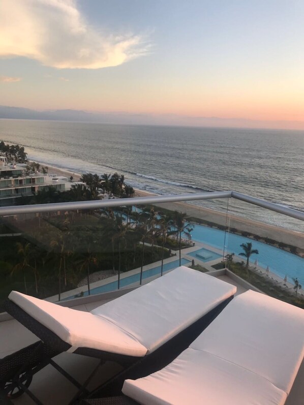 Enjoy stunning views of the beach and pool from this balcony, featuring two comfortable lounge chairs.