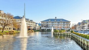 A calm water body with a fountain, surrounded by multi-story buildings with balconies and a clear sky.