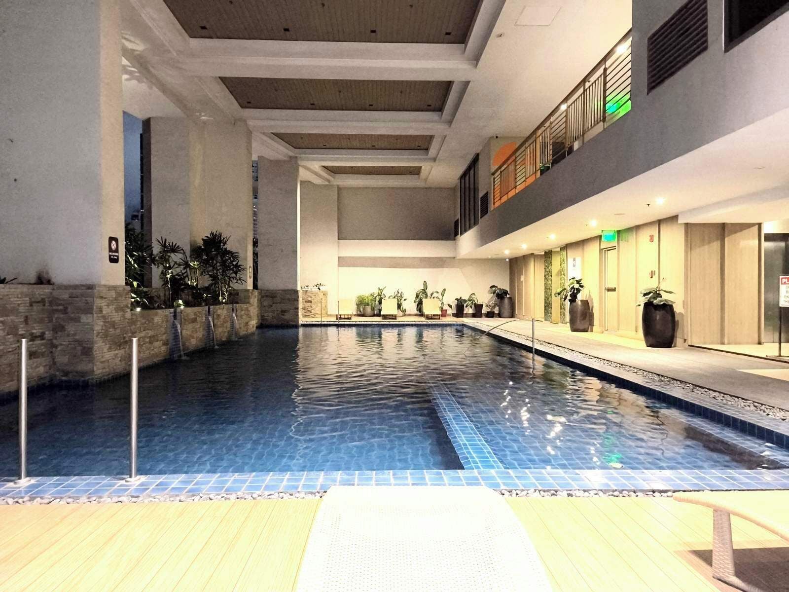 An indoor swimming pool with clear blue water, surrounded by stone walls and potted plants.
