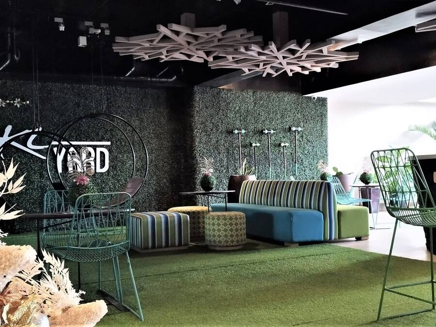 Un interior moderno con un sofá verde, sillas de metal y una pared decorativa con un diseño circular.