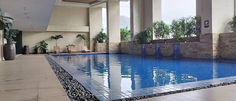 A swimming pool with a tiled edge, surrounded by potted plants and lounge chairs.