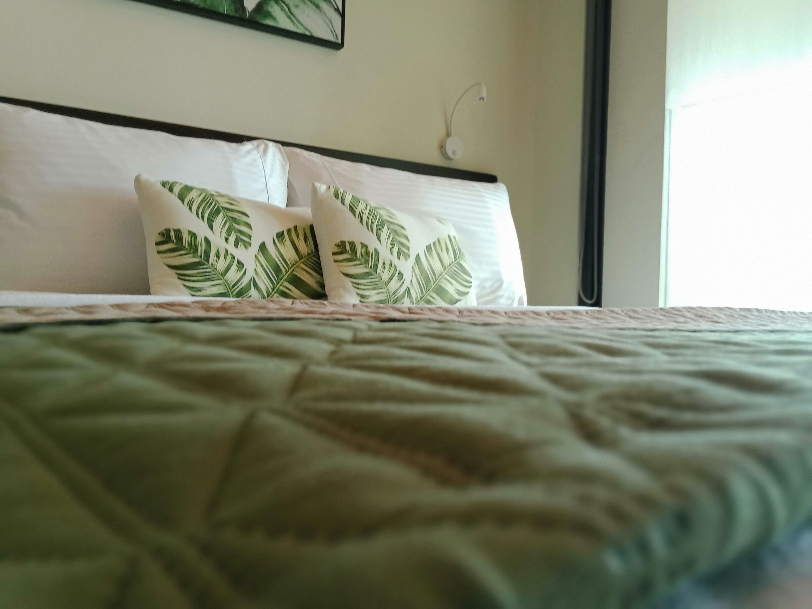 A bed with a green quilt and two pillows with a leaf pattern.