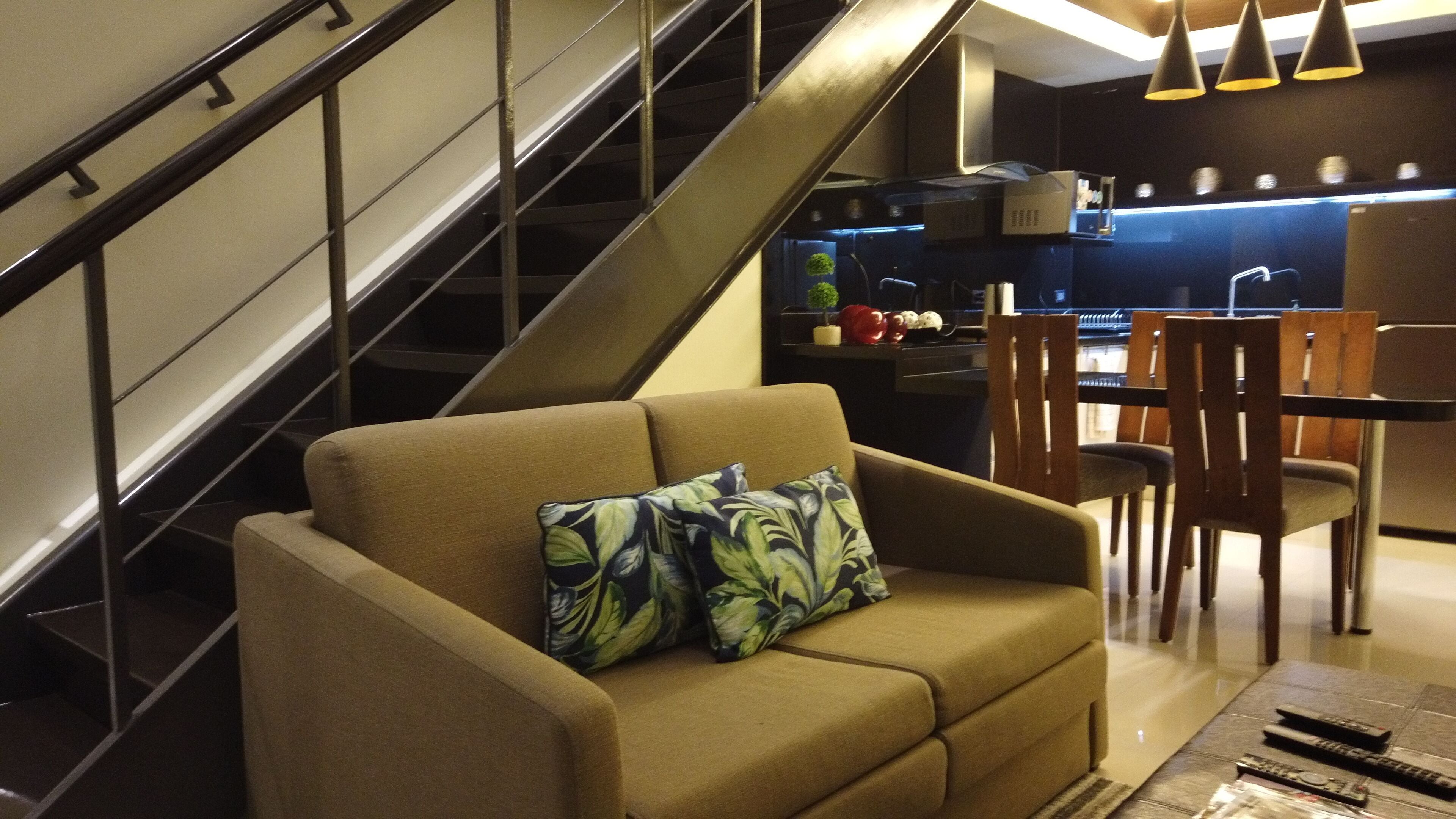 A modern living room with a sofa, a dining table, and a staircase.