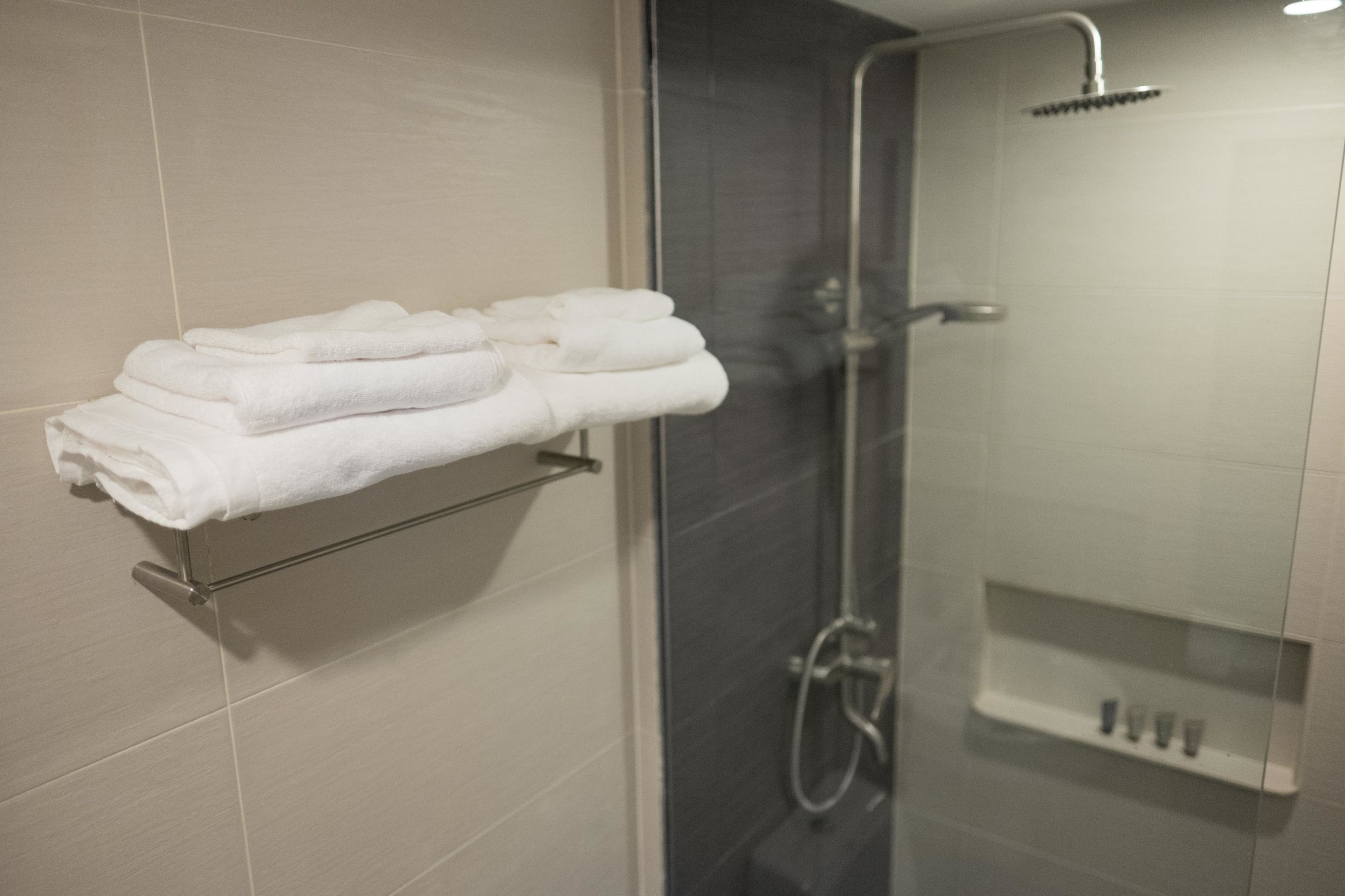 A bathroom with a glass shower enclosure, a towel rack with folded towels, and a small shelf with toiletries.
