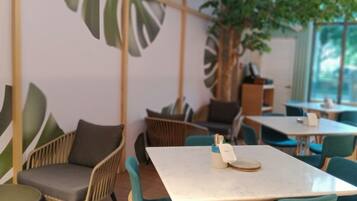 A modern cafe with wooden furniture, green chairs, and a large plant.