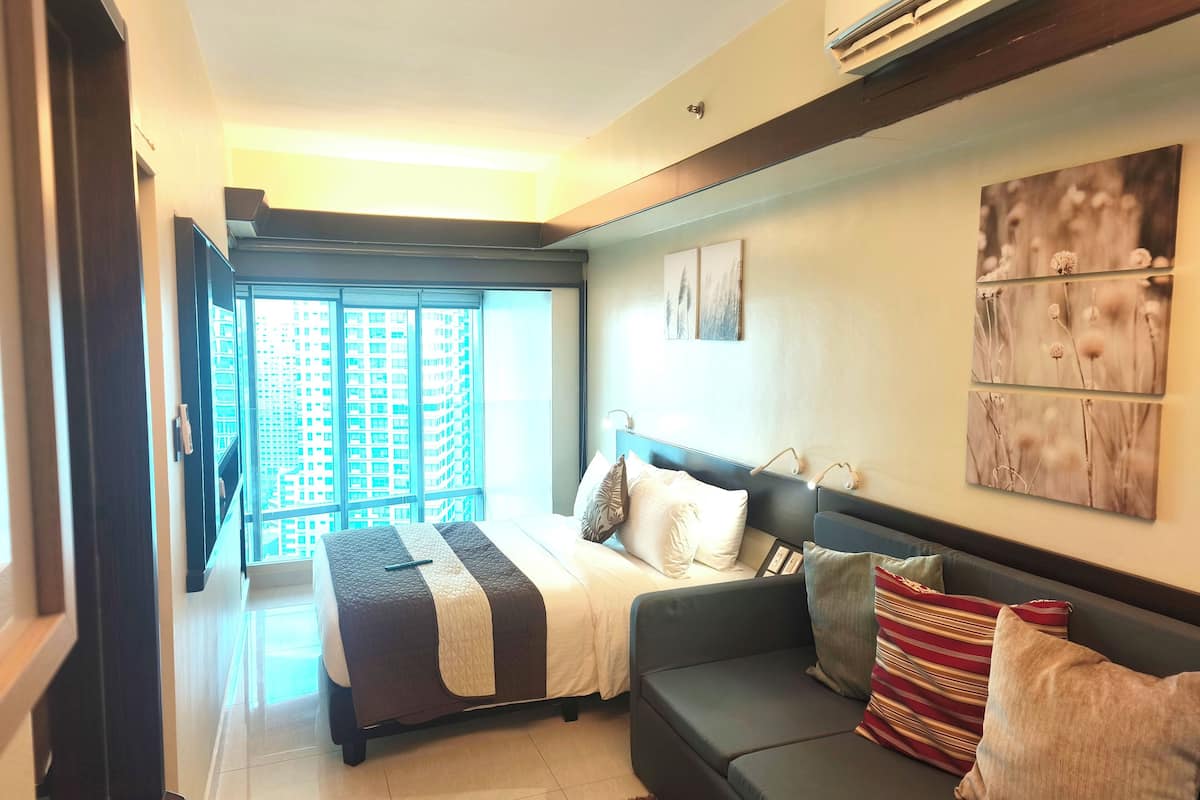 Quarto moderno com cama, sofá e uma grande janela com vista para a cidade.