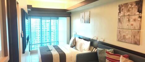 A modern bedroom with a bed, a sofa, and a large window offering a city view.