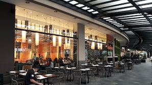 An indoor dining area with tables and chairs, a glass wall with reflections, and a ceiling with a skylight. - KL Executive Greenbelt KLX (Makati)