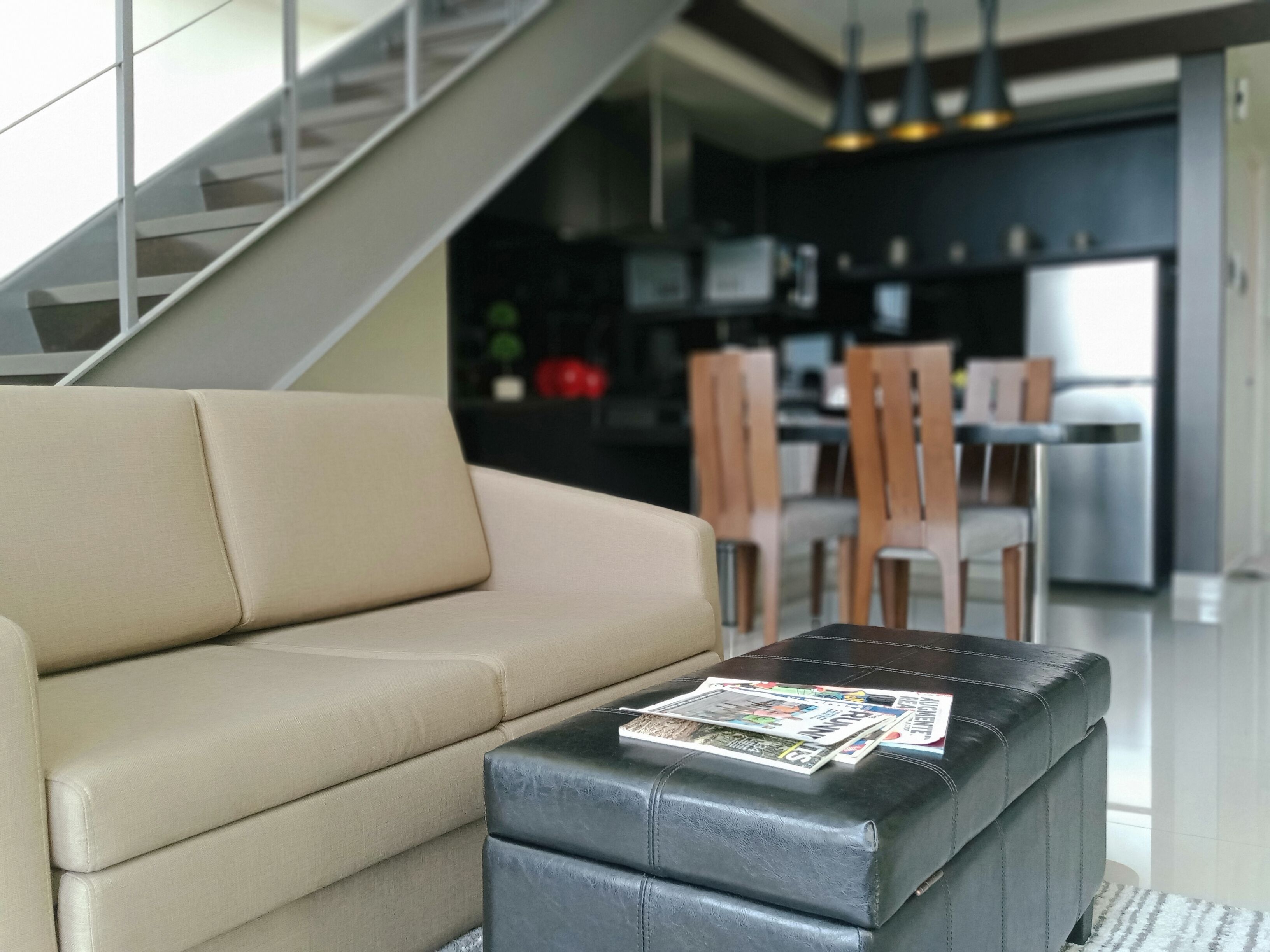 A modern living room with a sofa and a coffee table, a staircase leading to an upper floor, and a kitchen area in the background.