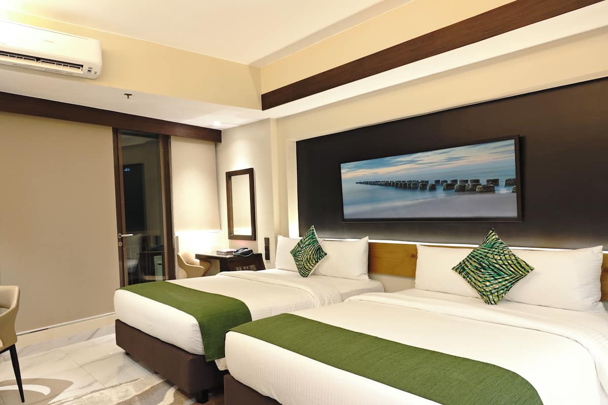 Quarto de hotel com duas camas, uma televisão na parede e uma secretária com uma cadeira.