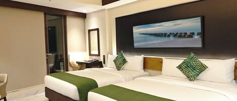 Quarto de hotel com duas camas, uma televisão na parede e uma secretária com uma cadeira.