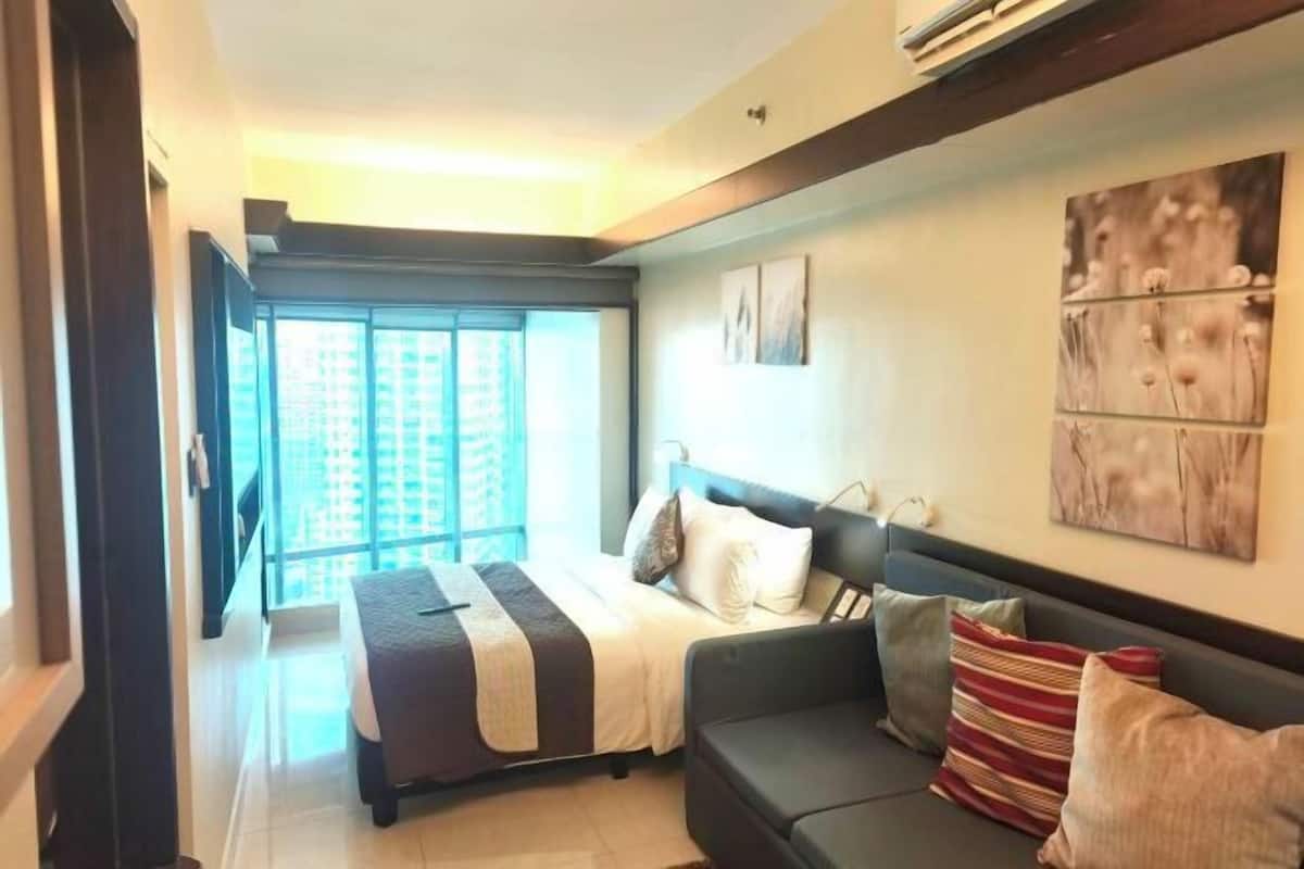 Quarto de hotel com cama, sofá, janela grande e obras de arte na parede.