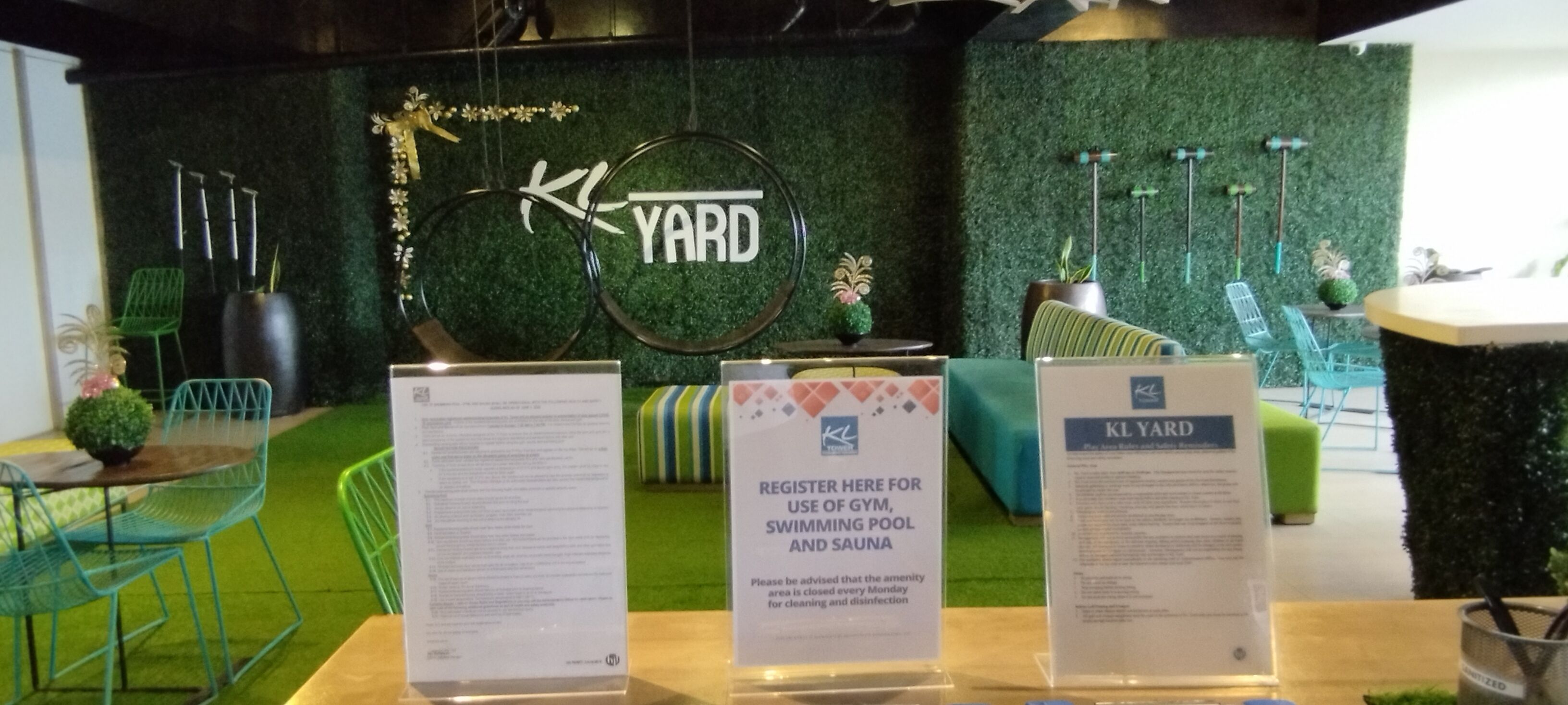 A reception area with a green artificial grass floor, a signboard with 'KL YARD' logo, and a registration desk.