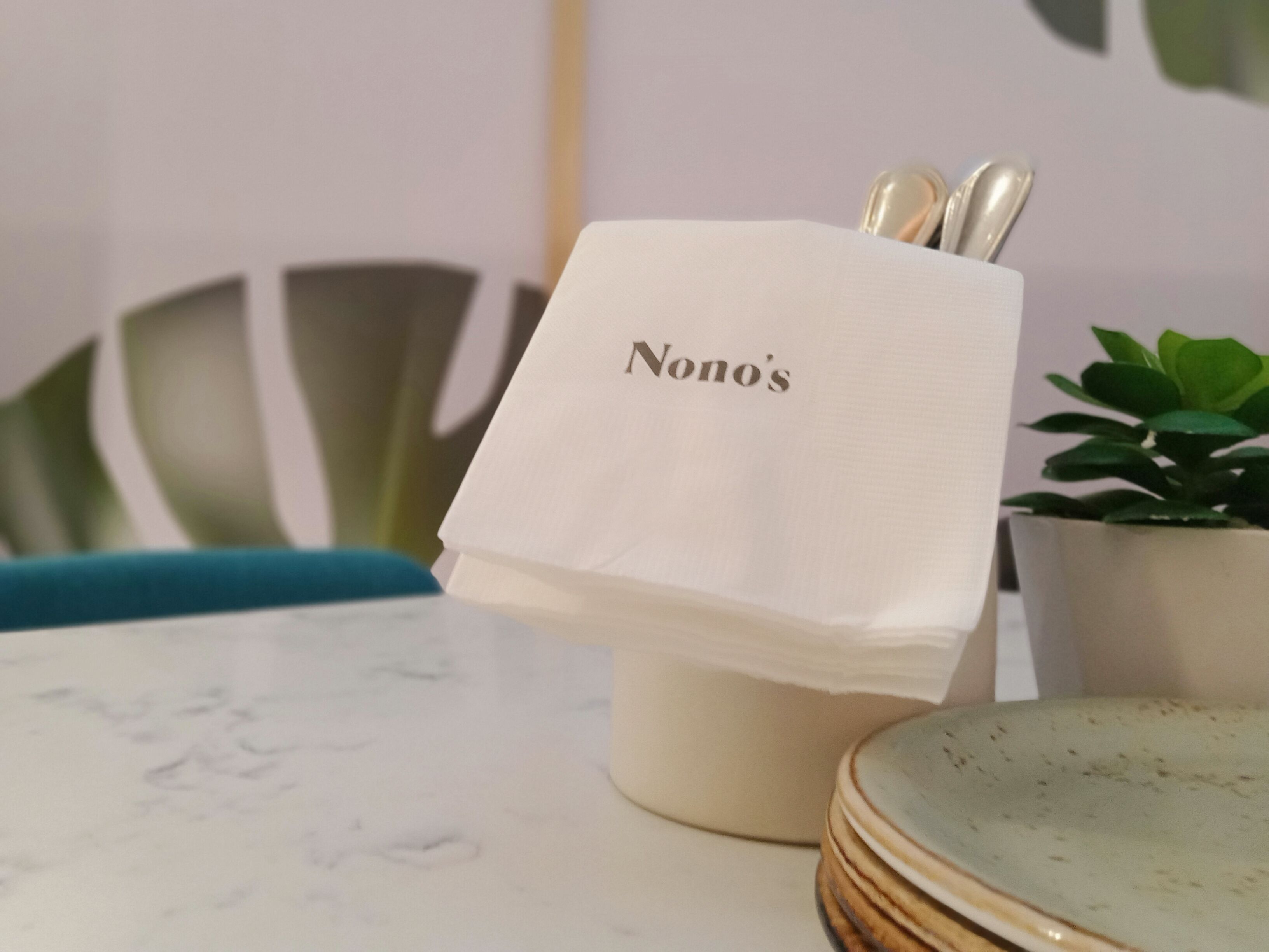 A table with a napkin holder labeled "Nono's" containing a spoon and a fork.