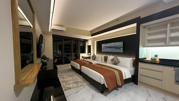 A modern hotel room with a large bed, a desk, a TV, and a view of the city at night. - KL Executive Greenbelt KLX (Makati)