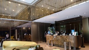 A modern lobby with a reception desk, seating area, and a high ceiling with unique lighting. - KL Executive Greenbelt KLX (Makati)