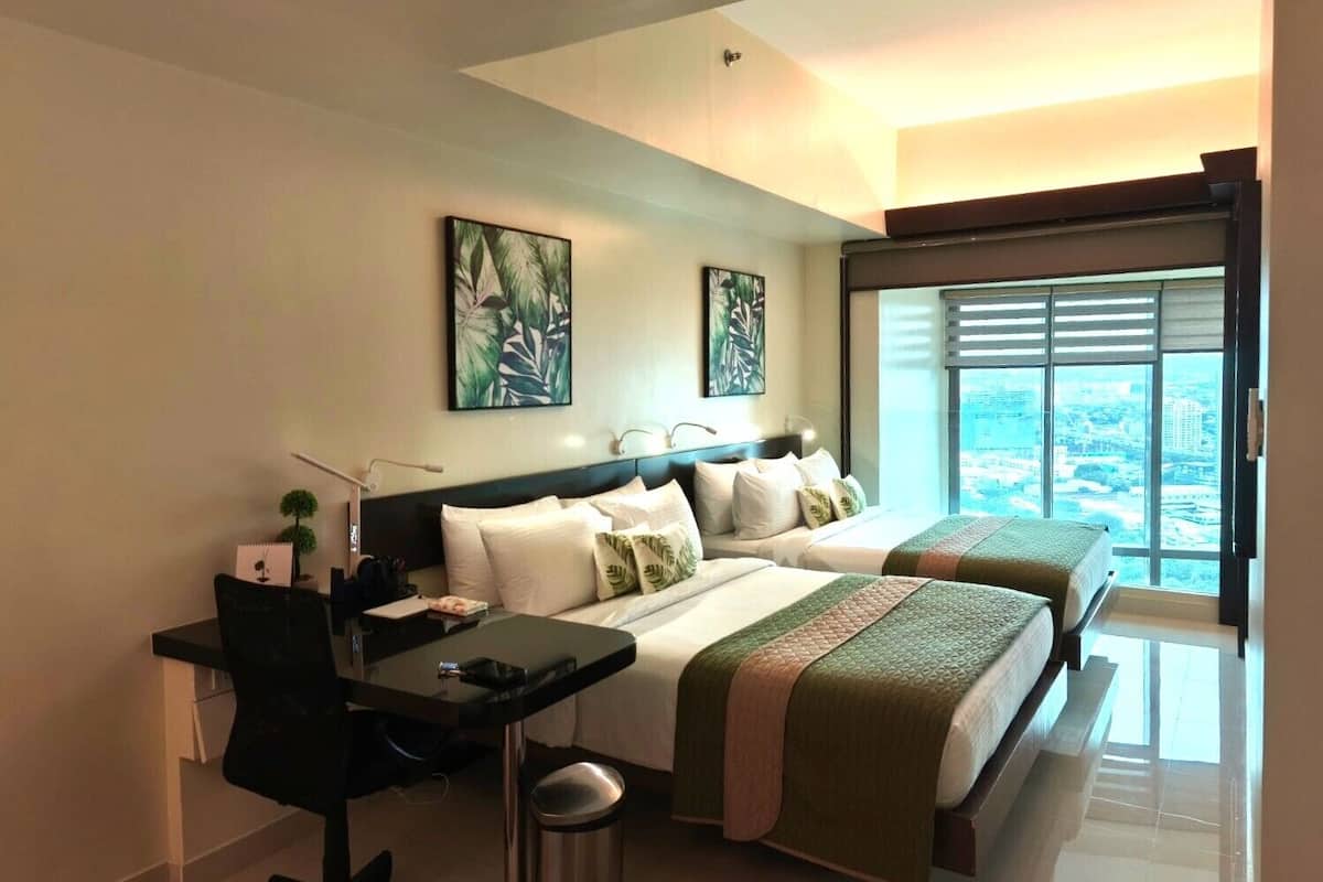 Quarto de hotel com duas camas, uma mesa e vista para a cidade.