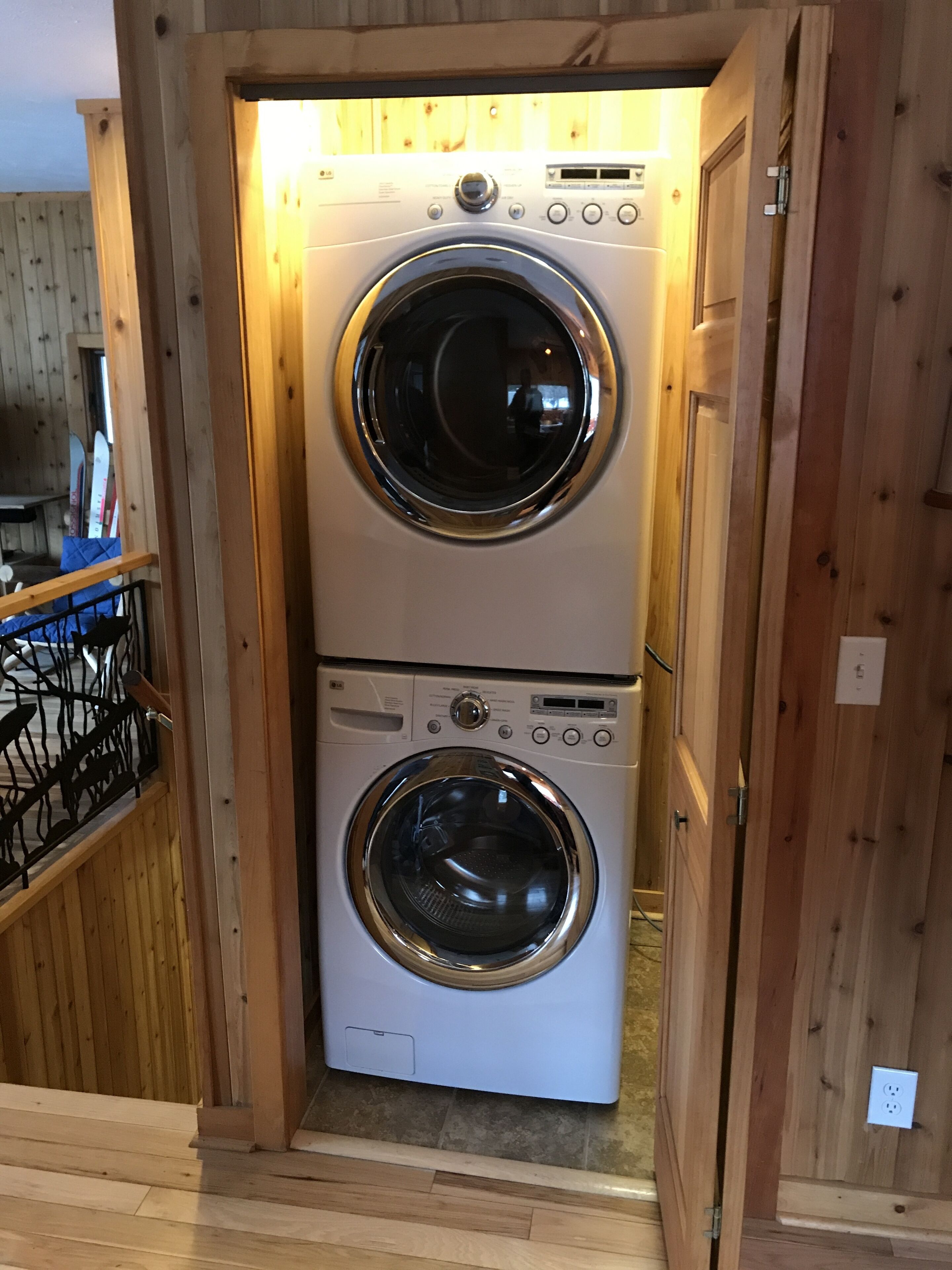 A laundry room with two stacked front-loading washing machines, wooden walls, and a metal railing.