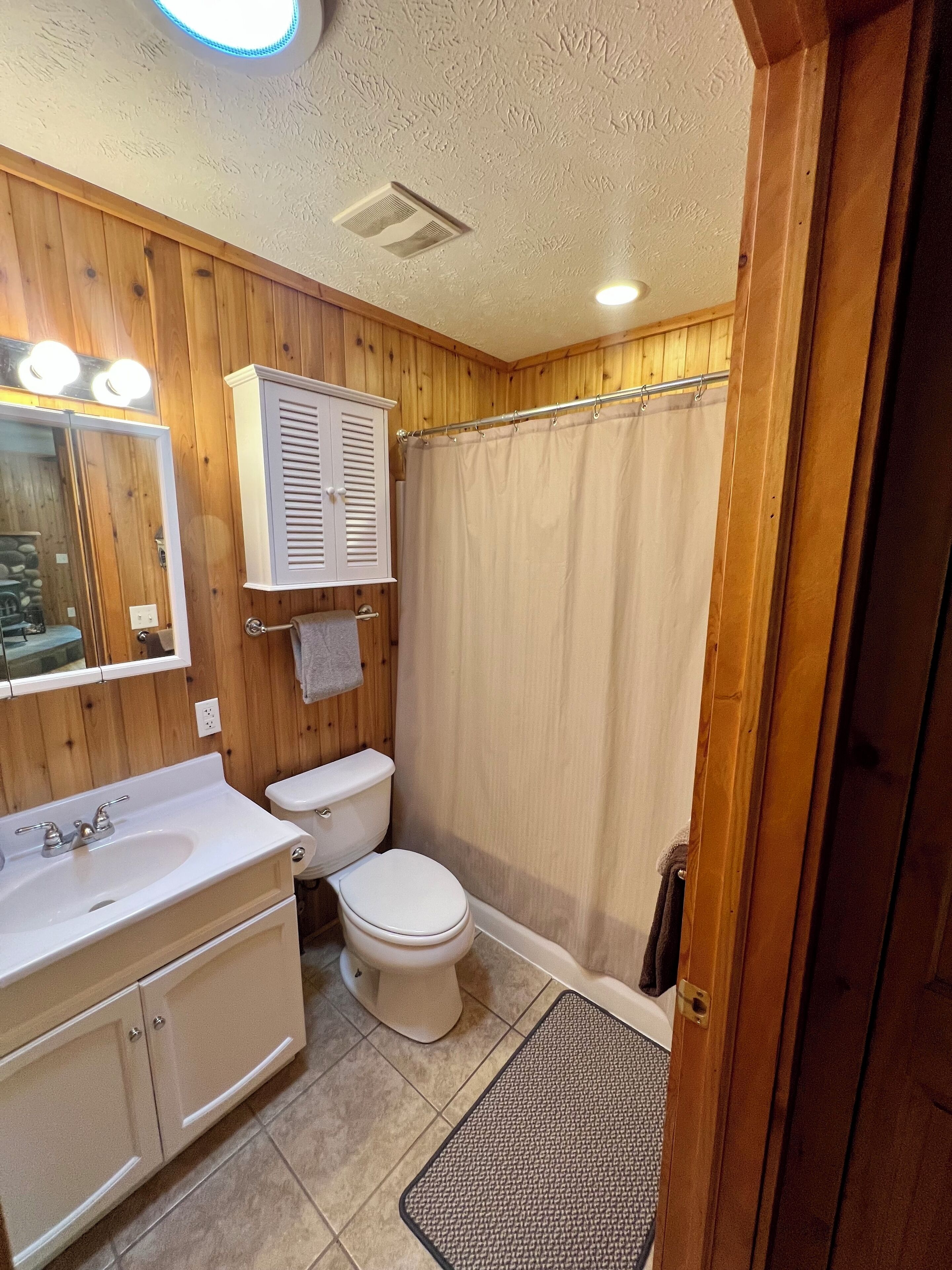 A bathroom with wooden paneling, a white sink, a toilet, and a shower curtain.