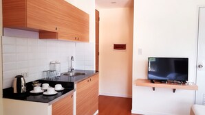 Una cocina compacta con armarios de madera, encimera negra, un lavabo y una estantería empotrada para la televisión.