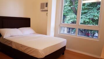 Una cama con ropa blanca en una habitación con ventana que da a un árbol.