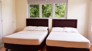 Two single beds with dark headboards in a room with a large window and a view of greenery outside.