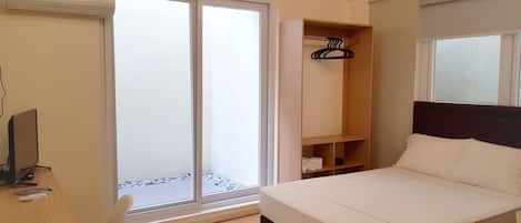Un dormitorio con cama, escritorio, silla, armario y puerta corrediza de vidrio que da a un balcón.