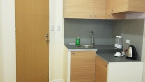 Una cocina compacta con armarios de madera, un lavamanos, un hervidor y un cubo de basura.