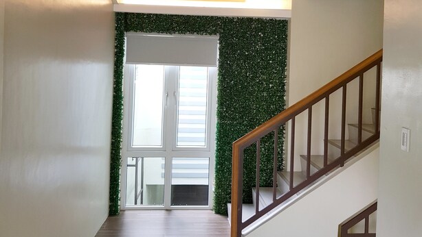 Un pasillo con techo de madera, una escalera con barandilla de madera y una pared verde con una ventana al final.