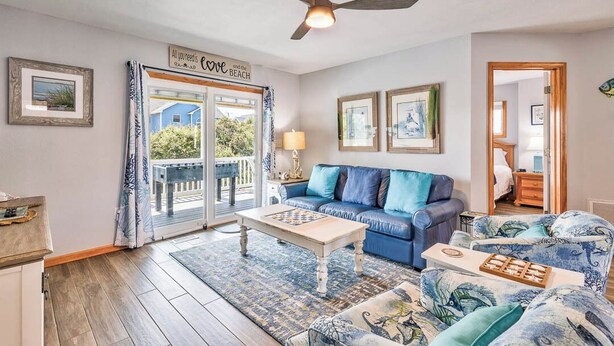 Un salon avec un canapé bleu, une table basse et un ventilateur de plafond. Il y a une pancarte sur la porte sur laquelle on peut lire : « Tout ce dont vous avez besoin, c’est de l’amour et de la plage. »