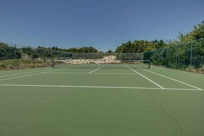 Un court de tennis en plein air, doté d’un filet, entouré d’une clôture et de verdure.