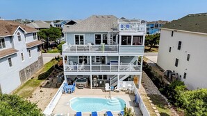 Une maison à plusieurs étages avec une piscine, un espace salon extérieur et un jardin clôturé.