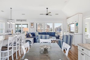 Eine moderne Küche mit weißen Schränken, ein Essbereich mit weißen Stühlen und ein blaues Sofa mit gestreifter Polsterung.