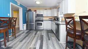 A compact kitchen with a refrigerator, oven, microwave, and sink. There are wooden chairs and a small dining table.