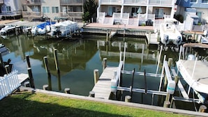 A marina with multiple boats docked, a grassy area in the foreground, and a building with balconies in the background.