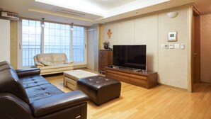 A spacious living room with a large flat-screen TV, leather sofas, a wooden coffee table, and a large window offering a view of the outdoors. - Gangnam Galaxy Apartment 1 (Seoul)