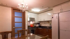 A modern kitchen with white cabinets, a stainless steel range hood, a refrigerator, and a dining table with chairs. - Gangnam Galaxy Apartment 1 (Seoul)