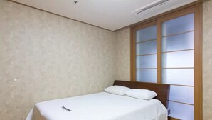 A single bed with a wooden headboard in a room with patterned wallpaper and a large window with frosted glass panels. - Gangnam Galaxy Apartment 1 (Seoul)