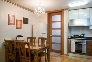 Un coin repas avec une table et des chaises en bois, un réfrigérateur, une cuisinière et un lustre.