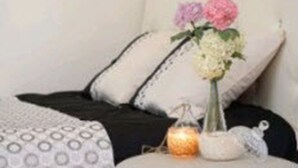 Een bed met een zwart-wit gebeddeken, een vaas met bloemen en een kleine kaars op een nachtkastje.