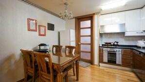 Een eetruimte met een houten tafel en stoelen, een kroonluchter en een keuken met witte kastjes en een fornuis.
