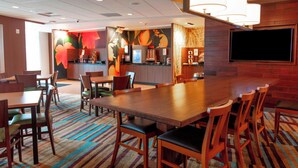 A hotel lobby with a long wooden table, several chairs, a coffee machine, and a TV mounted on the wall.