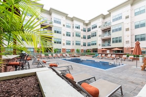 A rooftop pool area with lounge chairs and umbrellas, surrounded by a multi-story building with balconies. - Montclair Apartments by Gracen Properties (Montclair)