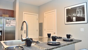 A modern kitchen with a stainless steel refrigerator, a built-in sink, and a granite countertop. There are two black mugs and a black plate on the counter. - Montclair Apartments by Gracen Properties (Montclair)