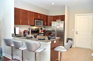 A modern kitchen with wooden cabinets, stainless steel appliances, and bar stools.