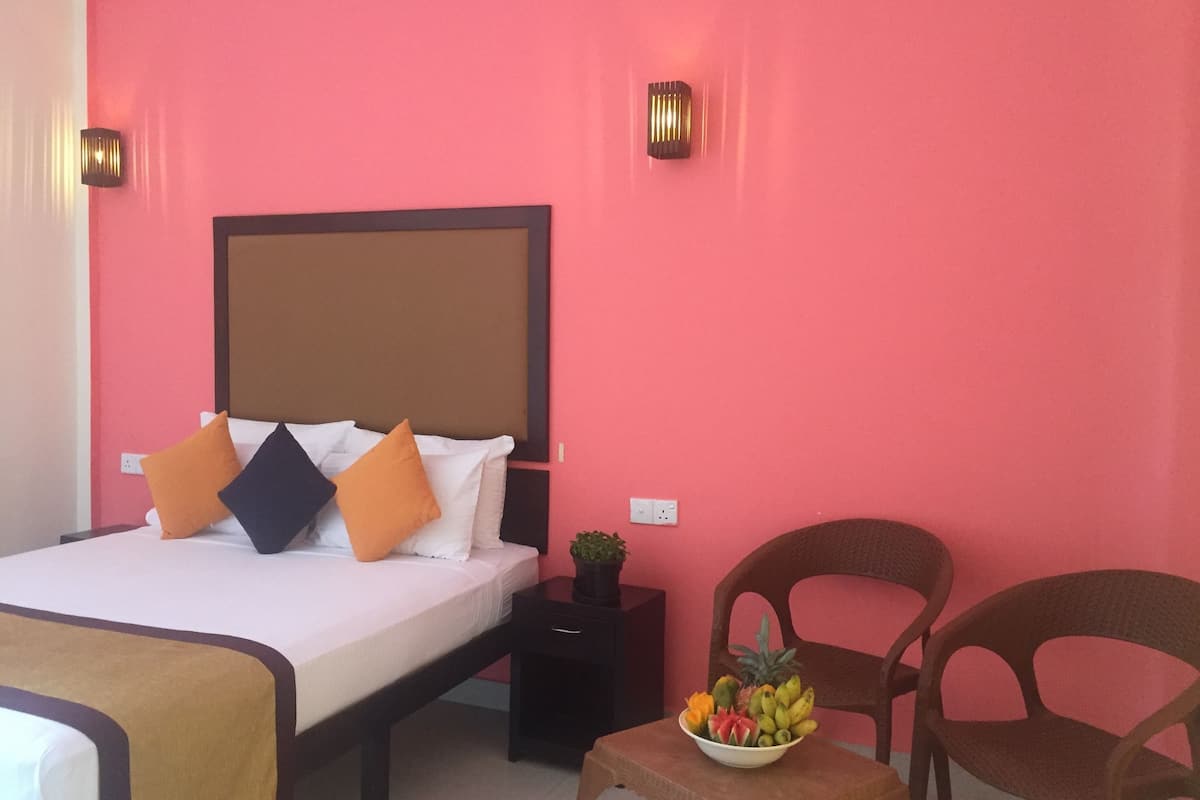 Une chambre d’hôtel avec un lit, une table de chevet, un panier de fruits et deux chaises.