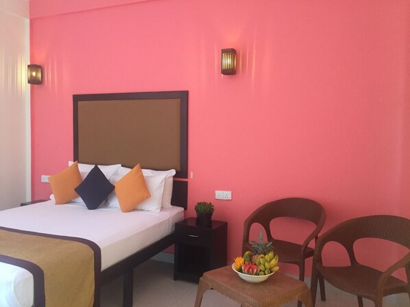 A hotel room with a bed, a nightstand, a fruit bowl, and two chairs.